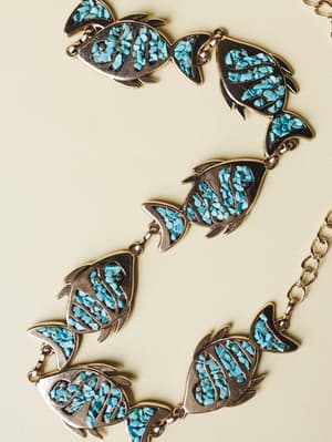 A vintage-inspired chain belt laid flat, featuring linked fish-shaped medallions filled with crushed turquoise stone set in gold-toned metal — earthy, a little wild, the kind of piece that makes an outfit feel like a story.