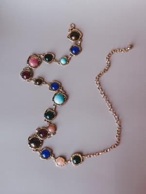A gold chain belt with multi-colored cabochon stones set in ornate bezels — the kind of piece that makes a simple dress feel like it has a whole personality.