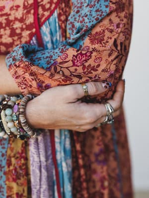 A close-up of stacked wrists and layered rings against a richly patterned mixed-print garment — the kind of detail shot that makes you want to dig through your jewelry box.