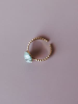 A dainty gold open-band ring with an engraved floral band and a small raw druzy stone center, shot solo against a soft lavender background — the kind of piece you put on without thinking and never take off.