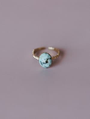 A delicate gold adjustable ring with an oval turquoise stone cabochon, shot clean against a muted lavender background — the kind of piece that looks like it was found at a market and worn every day since.