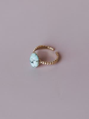 A dainty gold open-band ring with a beaded texture and an oval green stone centerpiece, shot overhead on a muted mauve surface — the kind of piece you'd reach for every single day without thinking twice.