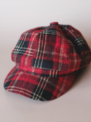 A red tartan newsboy cap shot up close against a soft neutral background — the kind of hat that makes a cozy fall outfit feel intentional.