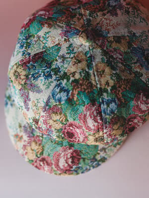 A close-up of a structured baseball cap made from a tapestry-style floral fabric — the kind of hat that looks like it wandered out of a vintage textile market and never looked back.