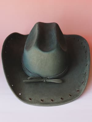 A worn-in olive suede cowgirl hat shot close against a soft blush backdrop — the kind of hat that already has a story before you put it on.