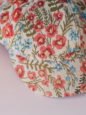 A close-up detail shot of a floral tapestry-style baseball cap laid on a soft lavender surface — the kind of hat that makes a casual outfit feel a little more intentional.