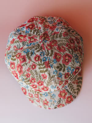A floral tapestry-style newsboy cap shot from above against a soft pink background — the kind of hat that makes a casual outfit feel intentional.