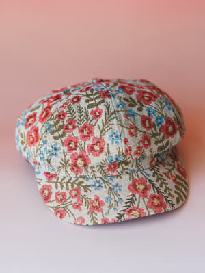 A floral tapestry newsboy cap laid casually on a soft pink surface — the kind of hat that makes a whole outfit feel intentional without trying too hard.