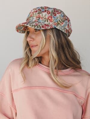 A floral tapestry baseball cap styled with a blush pink crewneck sweatshirt — the kind of hat that makes a casual outfit feel like it was actually thought about.