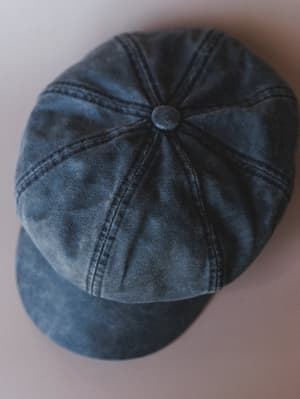 A washed black newsboy cap shot from above on a soft neutral surface — the kind of hat that makes a simple outfit feel intentional without trying too hard.