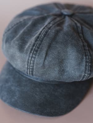 A close-up of a faded black newsboy cap with a worn, washed finish — the kind of hat that looks like it's already been on a few good adventures.