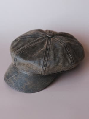 A worn-in leather newsboy cap in distressed brown sits against a soft gray studio backdrop — the kind of hat that looks like it already has stories.