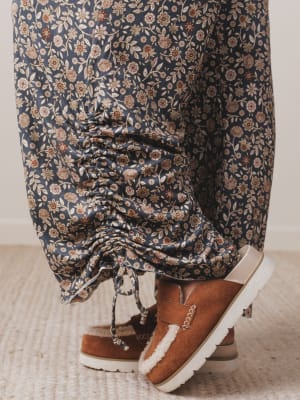 Person wearing floral pants and brown boots on a light wooden floor.