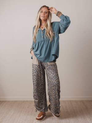 Woman wearing a blue top and patterned pants against a plain background
