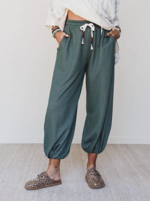 A relaxed mid-shot of cropped jogger pants in a washed two-tone olive green, styled with a cream textured top, stacked boho bracelets, and leopard print mules — the kind of outfit that looks effortless because it actually is.