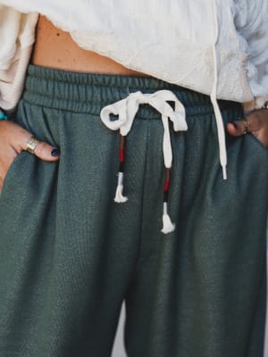 A close-up waist shot of wide-leg jogger pants in a washed two-tone olive, styled with a cropped cream top — the drawstring detail and relaxed drape do all the talking.