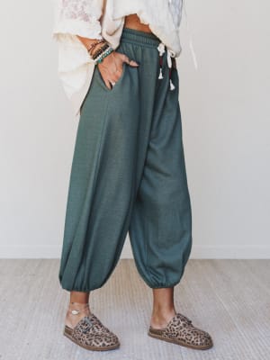 Relaxed harem-style jogger pants in a deep two-tone olive green, styled with a cream lace top, stacked bead bracelets, and leopard print clogs — the kind of outfit that looks effortless but is clearly very intentional.