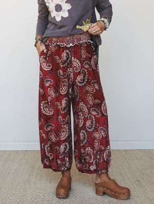 Wide-leg velvet pants in a rich burgundy paisley print styled with a washed graphic long-sleeve and wooden clogs — the kind of outfit that looks effortless but clearly has a point of view.