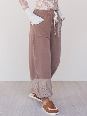 Person wearing brown ribbed pants with a white lace top on a light background