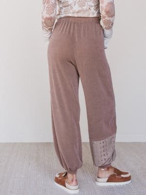 Person wearing brown ribbed pants with a white lace top on a neutral background