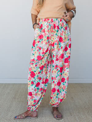 Flowy floral joggers in a bold garden print — red, yellow, and lavender blooms on white — styled with a peach tee and studded sandals for an effortlessly relaxed, color-happy look.