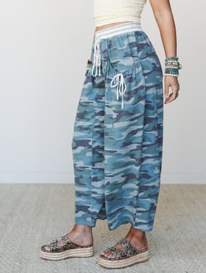 A relaxed wide-leg camo pant in cool blue-green tones styled with a cropped cream textured top, platform espadrille sandals, and a stack of beaded bracelets — the kind of outfit that looks effortless but is very much a whole vibe.