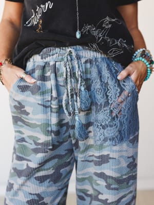 A close-up of blue camo ribbed joggers styled with a black graphic tee, the pants featuring a lace pocket detail and tassel drawstring that give them an unexpected boho edge.