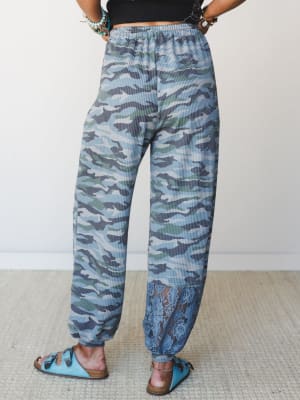 A back-view shot of relaxed camo joggers in a cool blue-green palette, finished with a surprise lace hem detail — the kind of pants that feel like sweats but look like a whole personality.