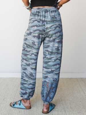 A back-view shot of relaxed camo joggers in a cool blue-green palette, finished with a surprise lace hem detail — the kind of pants that feel like sweats but look like a whole personality.