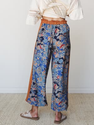 Shot from behind, this wide-leg floral pant in navy and cobalt blue with warm pumpkin side panels is styled with a cream lace crop top — the kind of outfit that feels effortless but clearly wasn't an accident.