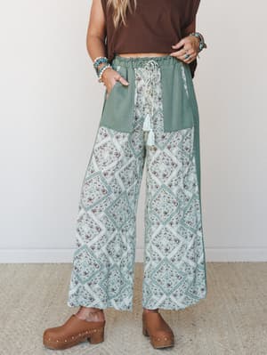 Wide-leg patchwork pants in sage and cream with a floral diamond print, styled with a cropped brown tee and wood clogs — the kind of outfit that looks effortless but definitely took thought.