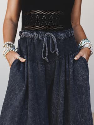 A close-up waist-down shot of a mineral-washed charcoal wide-leg pant styled with a black crochet top and stacked beaded bracelets — relaxed and a little undone in the best way.