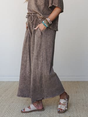 A relaxed, earthy set in mineral-washed mocha — wide-leg pants with a drawstring waist paired with a matching cropped tee, stacked beaded bracelets, and buckle sandals for that effortlessly put-together everyday look.