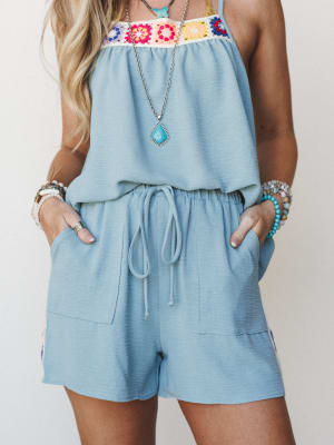 A light blue short romper with a colorful granny square crochet trim across the chest, styled with layered turquoise and beaded jewelry — easy, warm-weather boho with a handmade-feeling heart.