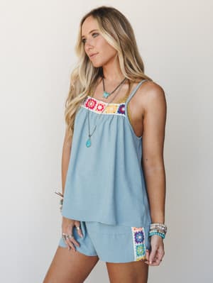 A flowy dusty blue tank and matching shorts set with colorful granny square crochet detailing — styled with layered turquoise necklaces and stacked bracelets for an effortlessly put-together warm-weather look.