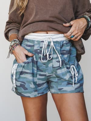 Relaxed camo drawstring shorts styled with a washed brown sweatshirt and layers of boho jewelry — the kind of effortless off-duty look that somehow still feels completely intentional.