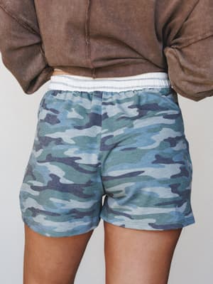 A back-view close-up of blue-toned camo pull-on shorts styled with a washed brown cropped sweatshirt — relaxed, lived-in, and the kind of outfit you wear when comfort is non-negotiable.