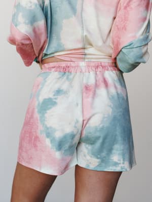 A close-up back view of a tie-dye matching set — pastel shorts with an elastic waistband paired with a matching cropped sweatshirt, all in a dreamy cotton-candy color wash.
