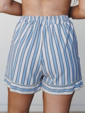 A close rear shot of relaxed high-waisted shorts in a soft blue, white, and black vertical stripe — the kind of easygoing piece that works just as hard on a beach boardwalk as it does on a lazy Sunday morning.