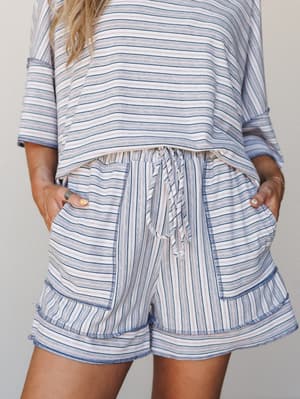 A close-up of a matching striped shorts set — the soft blue, pink, and white stripe pattern feels effortlessly relaxed, with the high-waisted drawstring shorts and patch pockets doing all the right things for a lazy-day-done-well kind of outfit.
