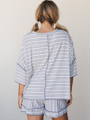 Shot from the back, a matching striped set in soft blue and cream — the oversized tee and easy shorts feel like the kind of outfit you'd never want to take off, styled with pearl hair ties that make the whole thing feel just put-together enough.