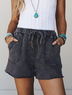 A mid-shot of acid-wash charcoal drawstring shorts styled with a white textured tank and stacked turquoise bracelets — casual and collected with just enough boho personality.