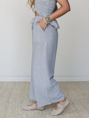 A side-profile shot of a striped smocked crop top and wide-leg ruffle-hem pant set styled with woven Mary Jane flats and stacked beaded bracelets — the kind of easy two-piece that feels pulled-together without trying too hard.