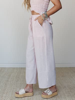 A sun-warmed side shot of wide-leg cropped pants in a soft pink stripe paired with a smocked crop top — the kind of effortless matching set that makes a Tuesday feel like a beach town.