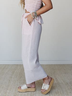 A side-profile shot of a striped rose and white matching set — smocked crop top with a ruffle hem and wide-leg pants — styled with stacked beaded bracelets and platform espadrille slides for an easy, warm-weather feel.