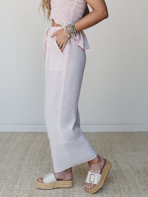 A side-profile shot of a striped rose and white matching set — smocked crop top with a ruffle hem and wide-leg pants — styled with stacked beaded bracelets and platform espadrille slides for an easy, warm-weather feel.