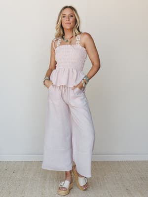 A breezy matching set in soft pink stripe — smocked cami top with daisy-trimmed tie straps and wide-leg cropped pants styled with layered beaded jewelry and platform espadrilles, giving off easy summer afternoon energy.