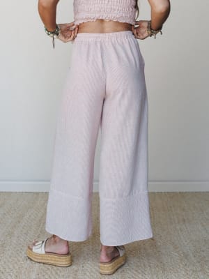 A back-view shot of wide-leg striped pants in a soft rose and white pinstripe, paired with a matching smocked crop top and espadrille platform sandals — easy, breezy, and made for somewhere warm.