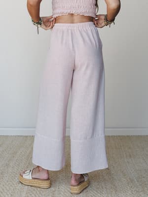 A back-view shot of wide-leg striped pants in a soft rose and white pinstripe, paired with a matching smocked crop top and espadrille platform sandals — easy, breezy, and made for somewhere warm.