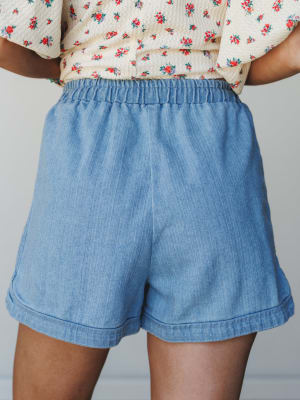 A back-view close-up of relaxed chambray shorts with an elastic waistband, styled with a floral print cropped top — easy, warm-weather dressing that feels effortless without trying.